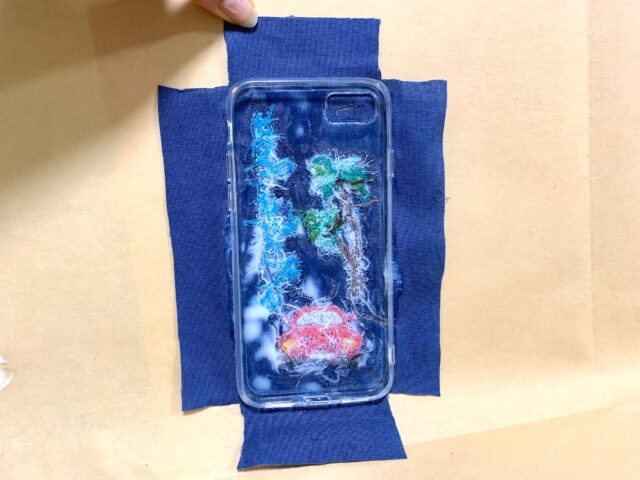 ボンドを付けたスマホケースを布にはり、その布の端を切った画像。